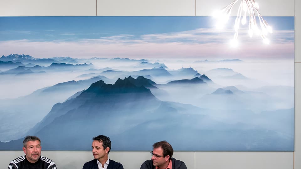 Drei Männer vor einem Bild mit Alpenpanorama