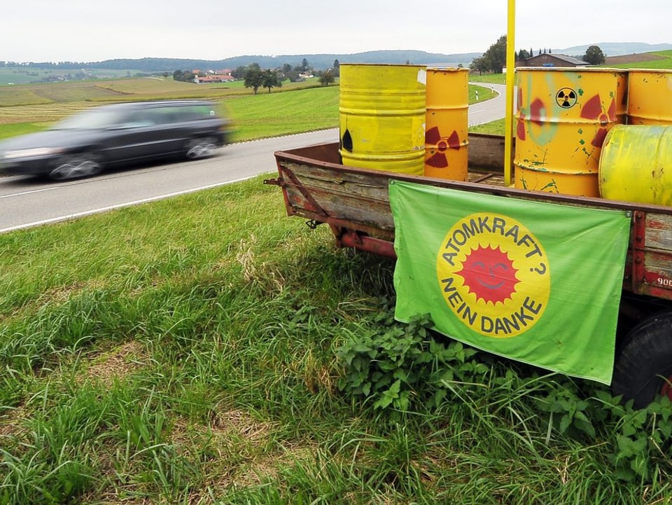 Autoanhänger mit gelben Atomfässern an einer Landstrasse, Flagge "Atomkraft, nein Danke"