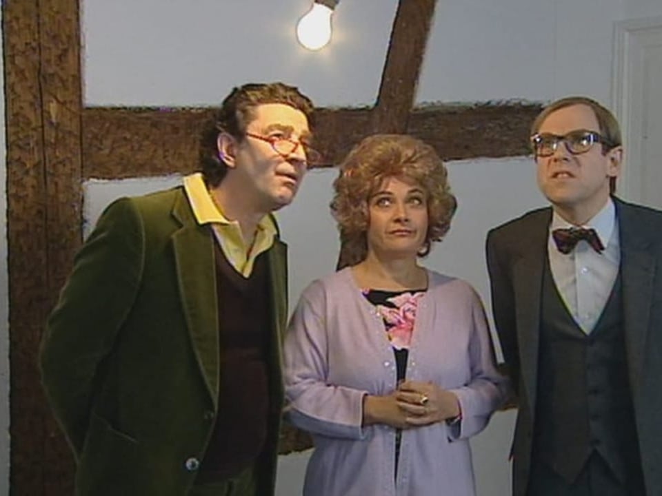 Zwei Männer und eine Frau stehen nebeneinander. Sie haben den Blick nach oben gerichtet, wo eine Glühbirne hängt..