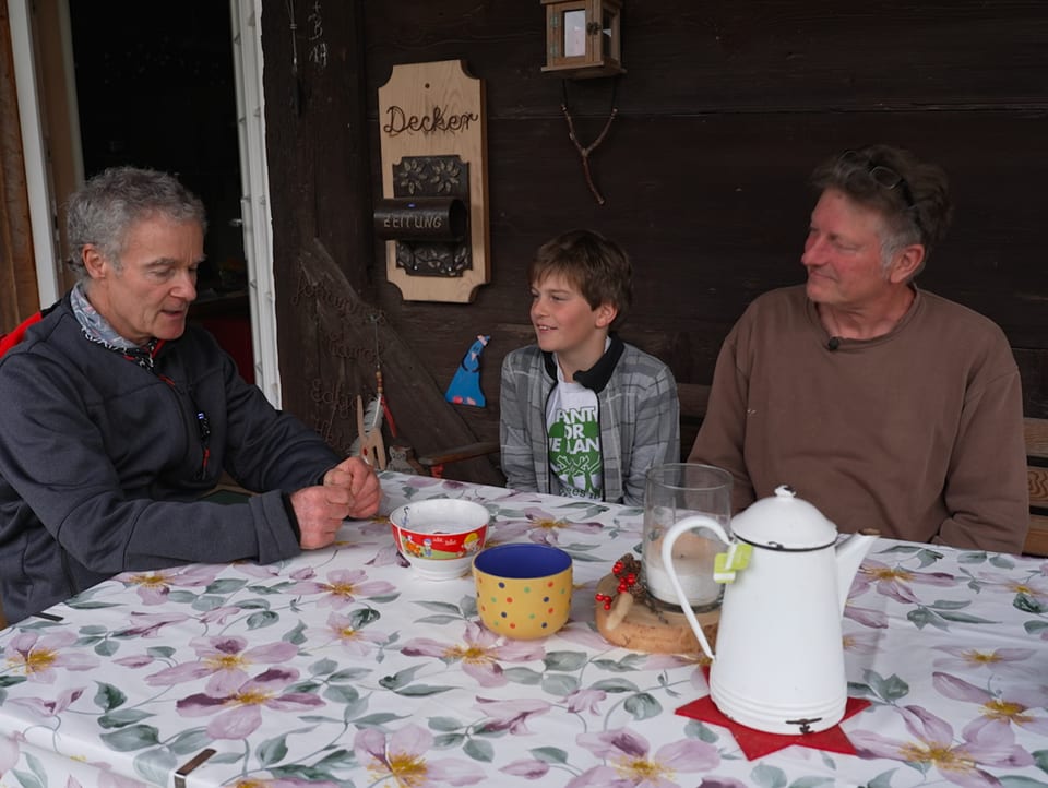 Hanspeter Bäni sitzt als Gast bei einem Mann und dessen Sohn.