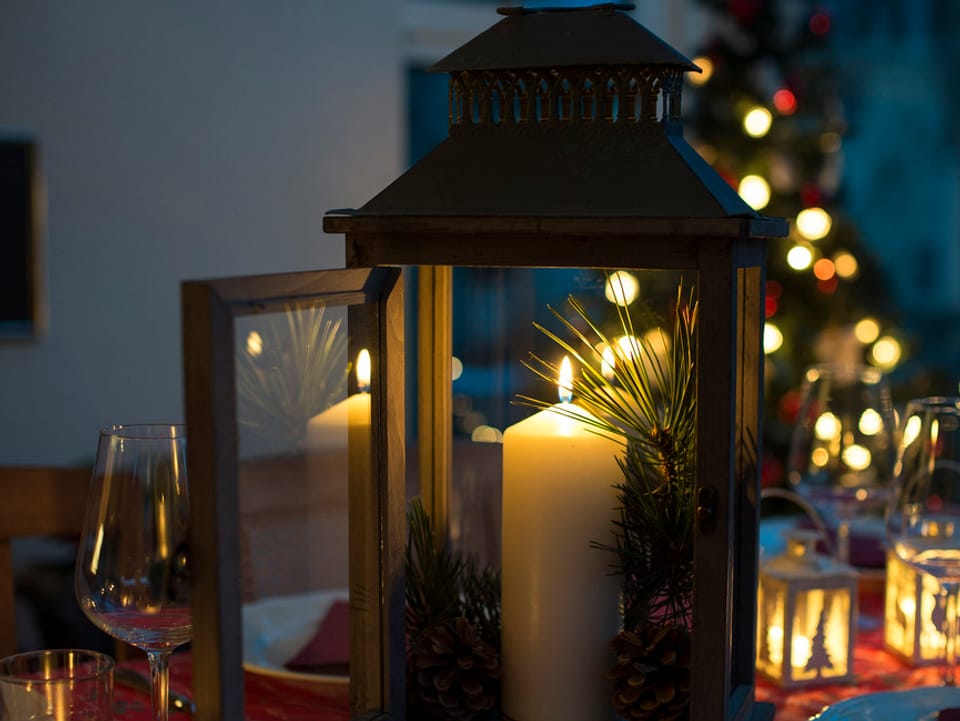 Ein weihnachtlich dekorierter Tisch mit Kerze und Weihachtsbaum im Hintergrund. 