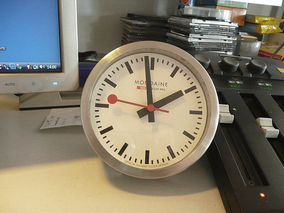 Grosse Uhr auf dem Schreibtisch neben dem Computer-Bildschirm.