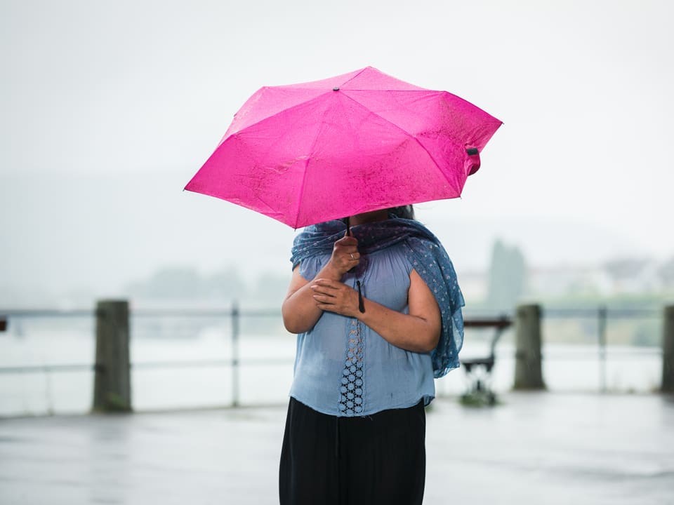 Eine Frau hält einen pinken Regenschirm in der Hand. Man sieht ihr Gesicht darunter nicht.