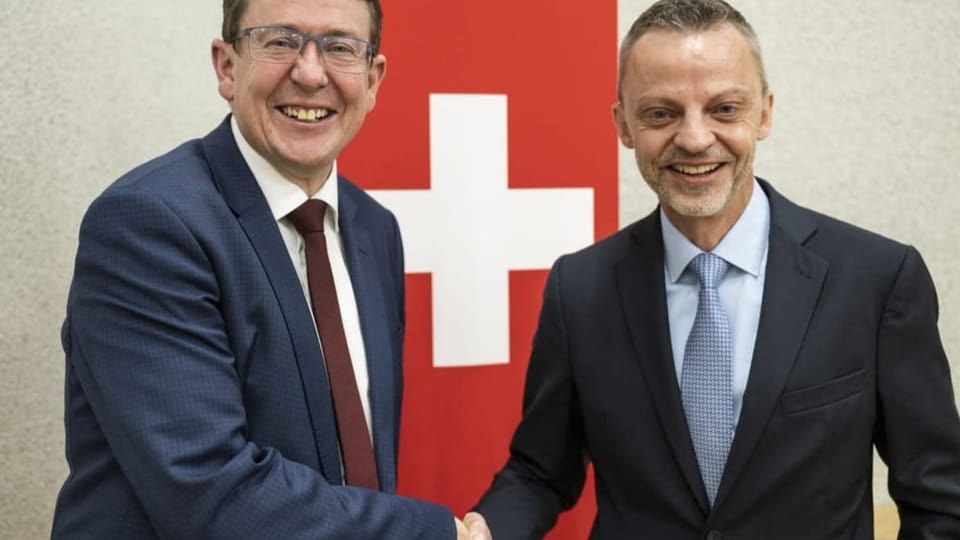 SVP Kandidat Albert Rösti und Herausforderer Hans-Ueli Vogt beim Hand-Shake vor einer Schweizerfahne