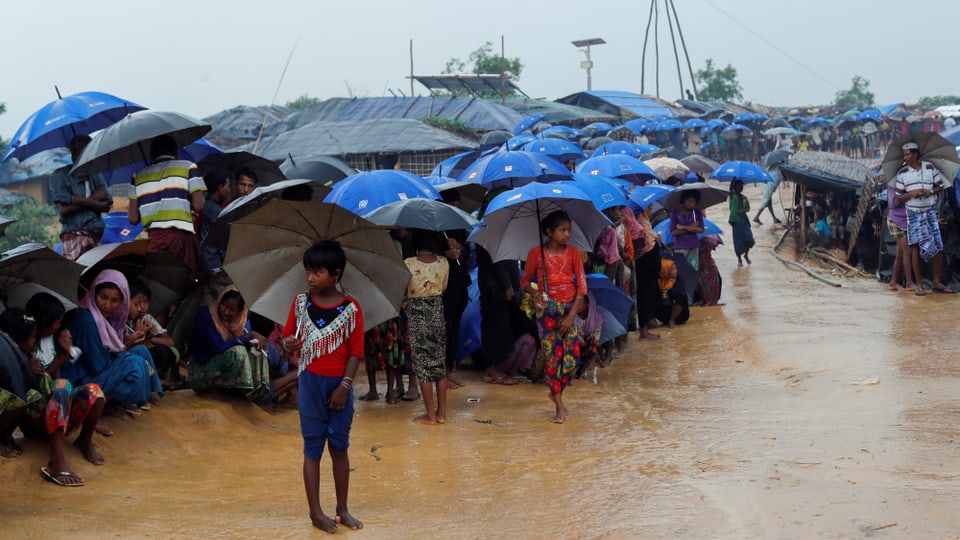 Menschen im Regen unter blauen Regenschirmen.