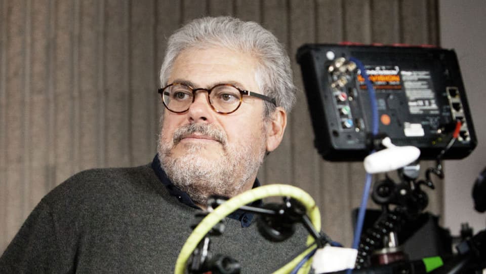 Roberto Andò mit Brille und schwarzen Pulli, neben einer Kamera.