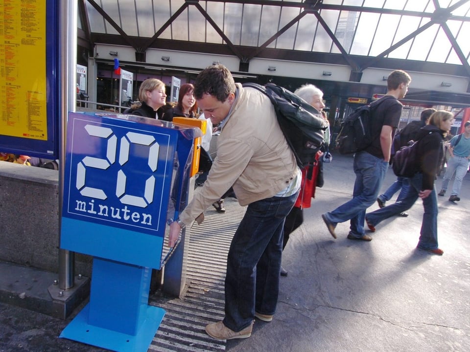 Ein Mann steht vor einer blauen 20-Minuten-Box und zieht sich ein Exemplar der Zeitung raus.