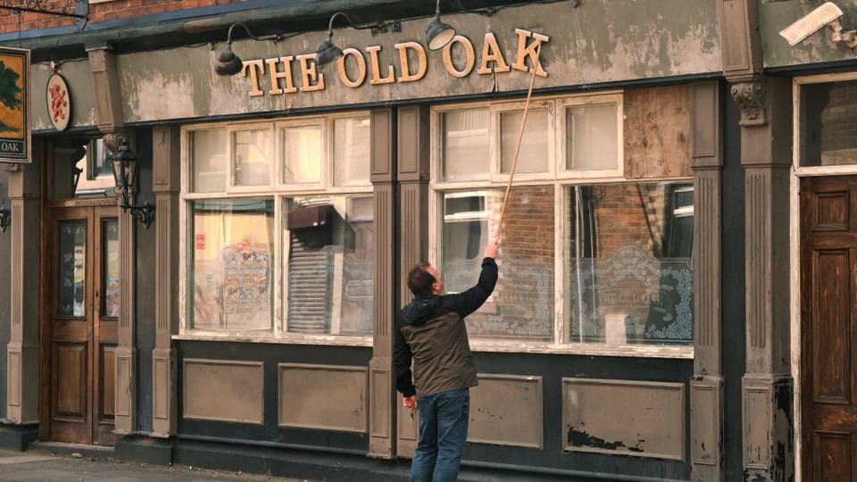 A man stands in front of a pub and tries to straighten a letter