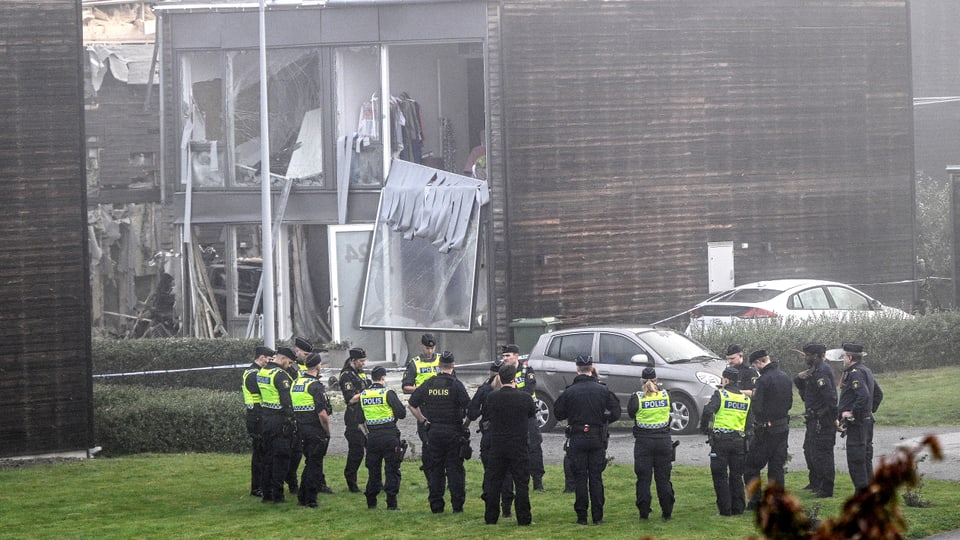 Mehrere Polizeibeamte stehen auf der Wiese vor einem zerstörten Wohnhaus  nahe Uppsala.