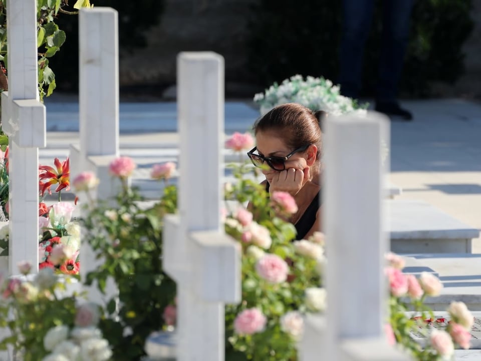 Eine Frau trauert an einem Grab mit einem weissen Kreuz.