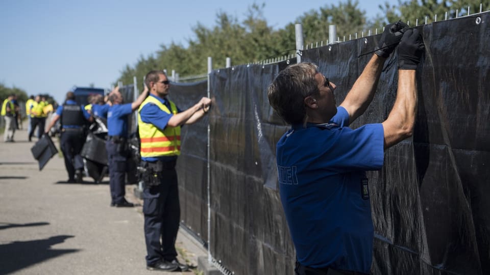Polizisten befestigen eine schwarze Plane an ein Gitter