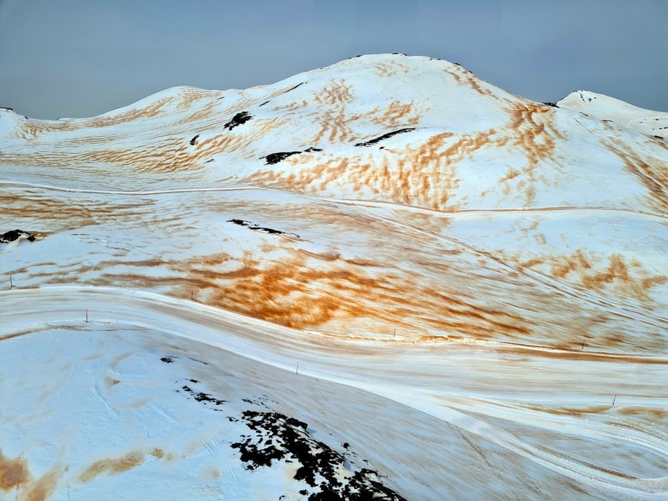 Schneebedeckte Berg mit braunem Saharastaub darauf.