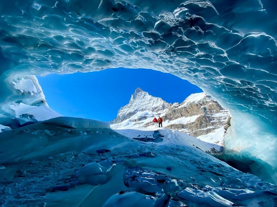Zwei Personen stehen ausserhalb der Gletscherhöhle.