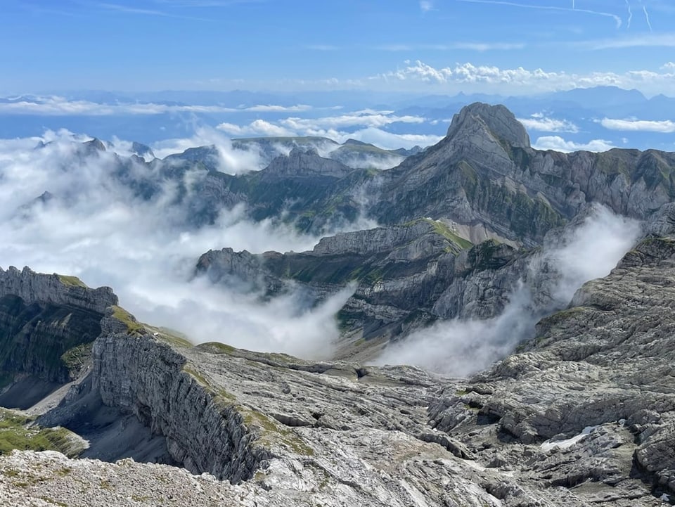 An alpine area with low, turbulent clouds like waves between the rocks. 