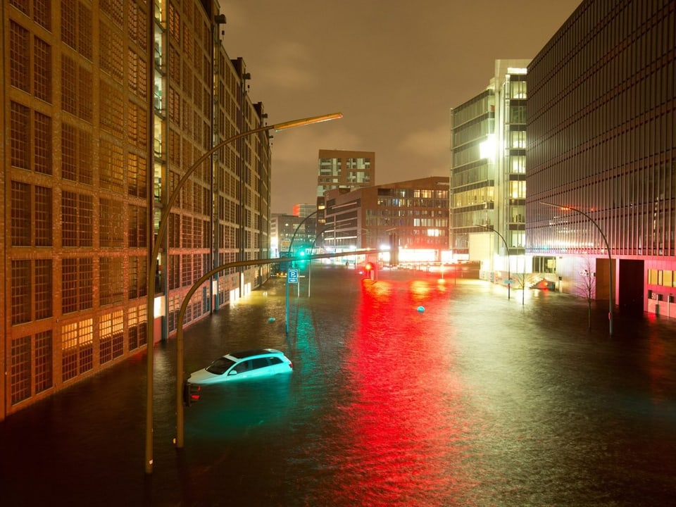 Ein überschwemmtes Hamburg in der Morgendämmerung, ein Auto schwimmt in der Flut durch die Stadt. 