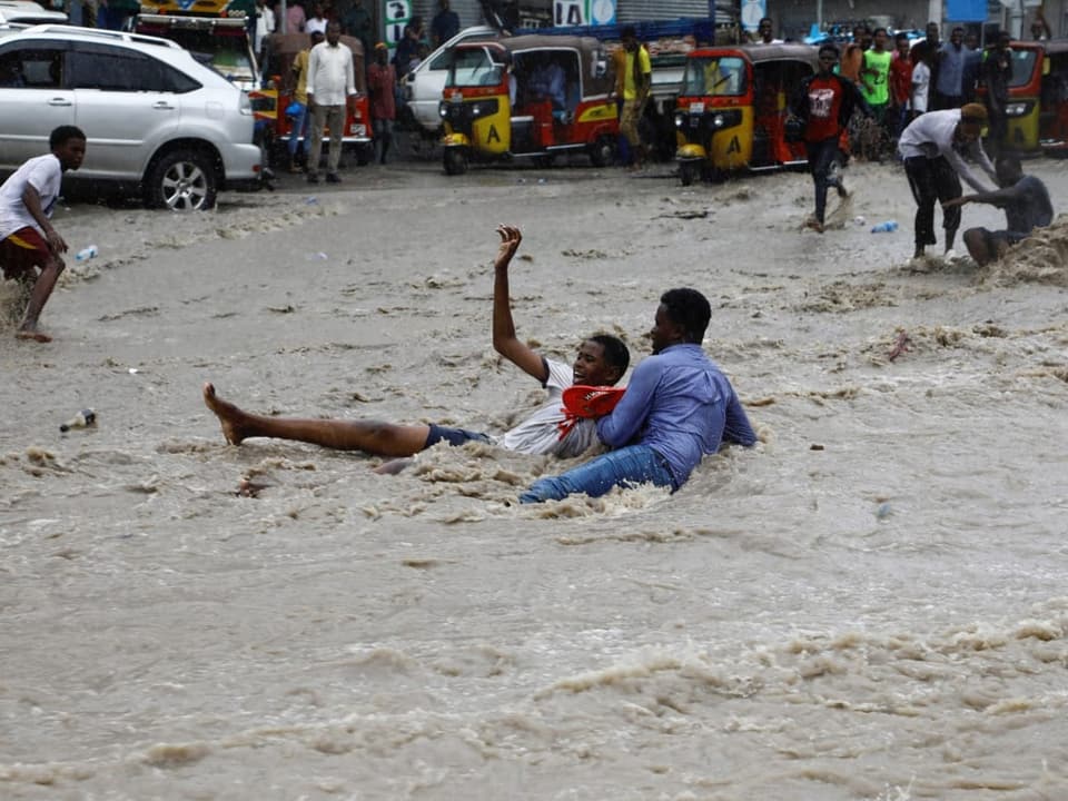 Personen liegen auf einer Strasse, die von Wassermassen überflutet wird.