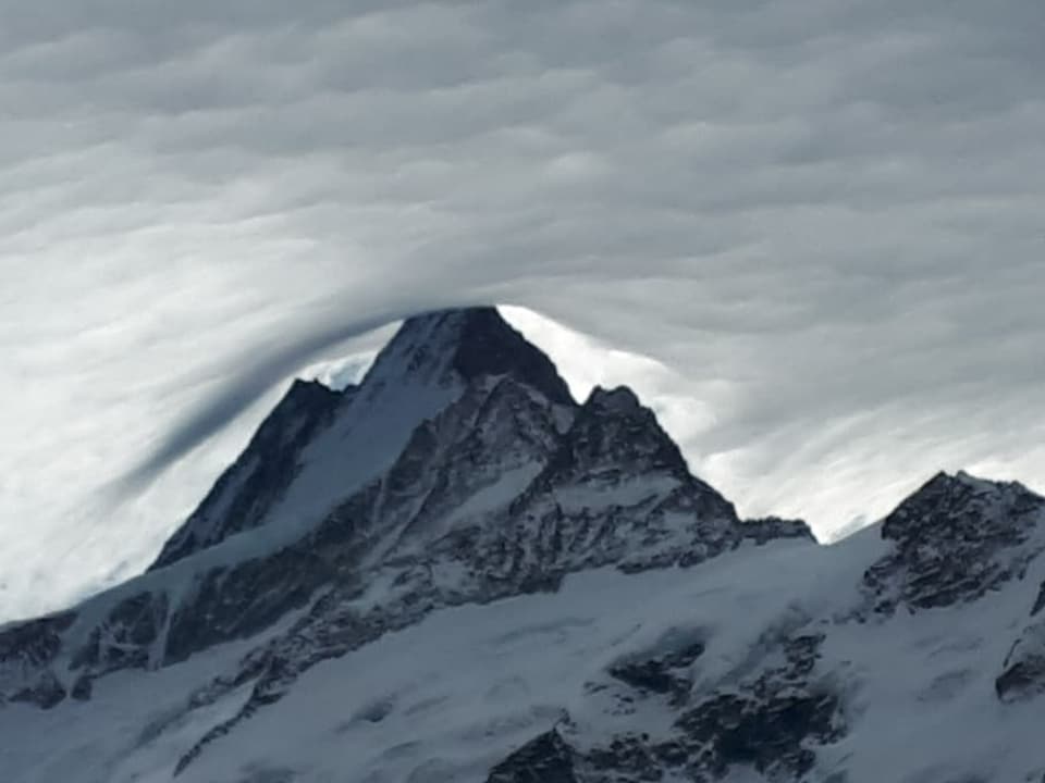 Schroffe Schneeberge mit Wolkendecke darüber. Um den Gipfel scheinen die Wolken angehoben. 