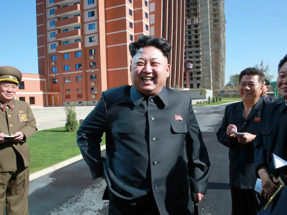 Kim lacht in die Kamera, daneben zwei Männer.