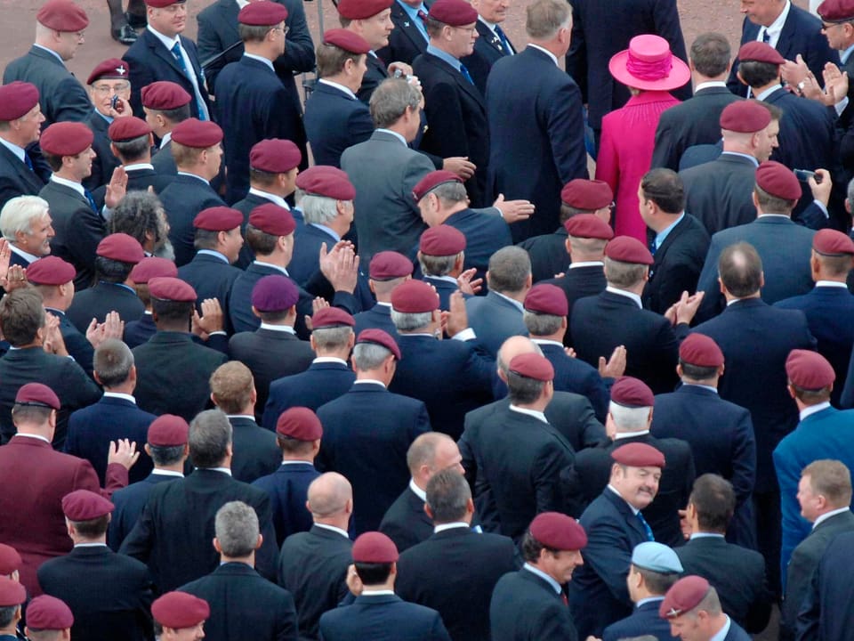 Eine Gruppe von dunkel gekleideten Veteranen und Margaret Thatcher – in Pink.