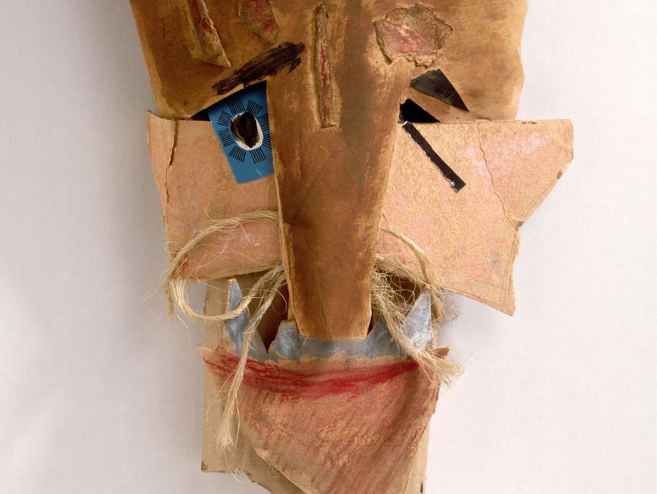 Eine Maske aus Papier, Karton und Farbe, um die Nase hat es Schnüre.