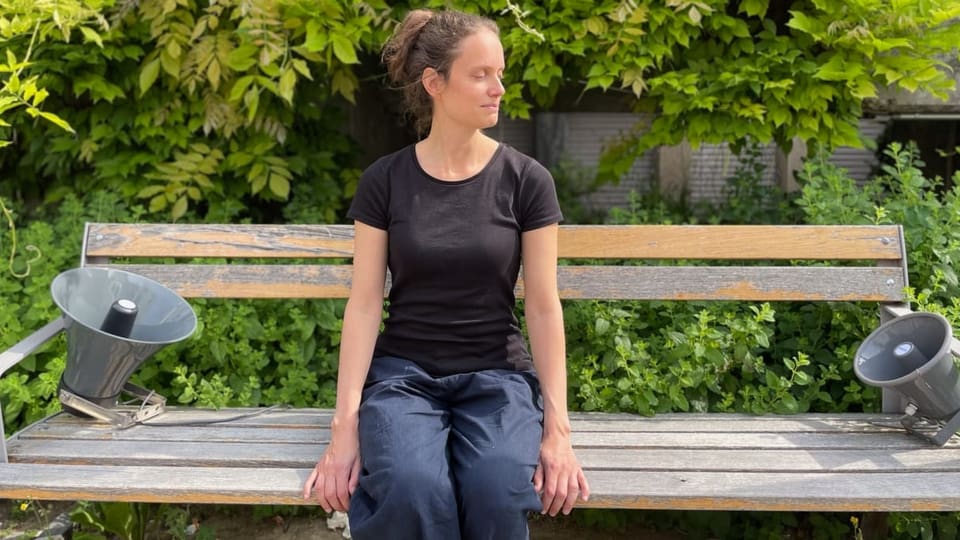 Eine Frau sitzt auf einer Bank, neben ihr zwei grosse Lautsprecher