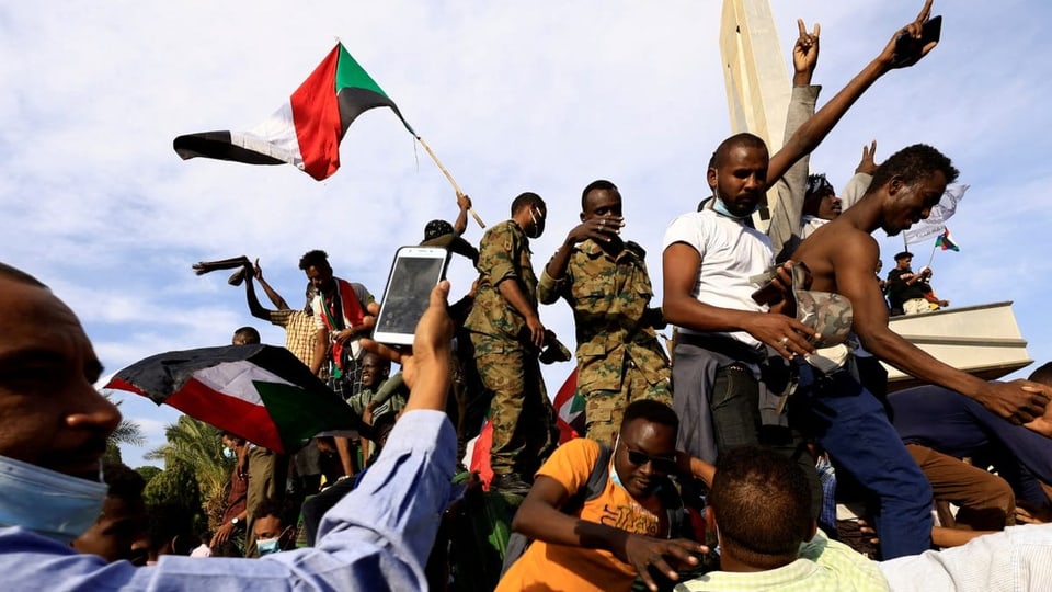 Menschen in Sudan protestieren, einer schwingt eine Flagge des Landes.