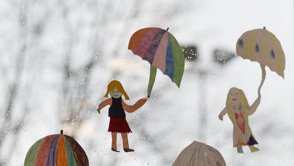 Papierfiguren mit Schirm vor verregneter Fensterscheibe.