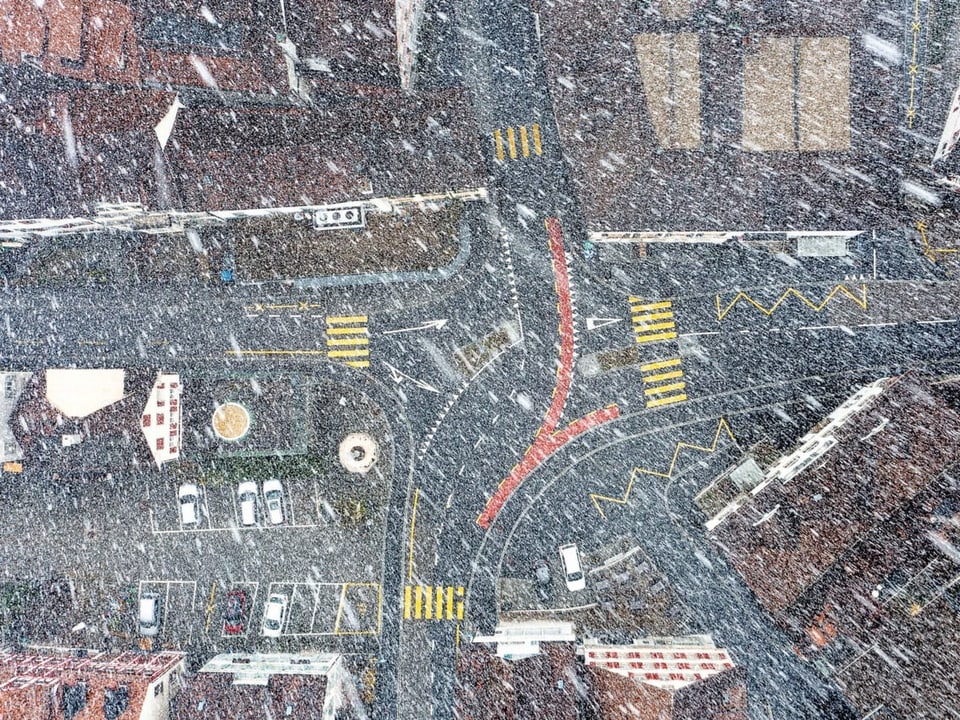 Aus der Vogelperspektive schaut man auf eine Stadt und sieht eine Kreuzung im Schneetreiben.