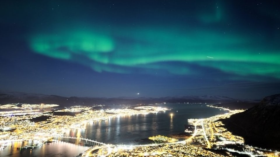 Grünes Polarlicht über dem Lichtermeer einer Stadt