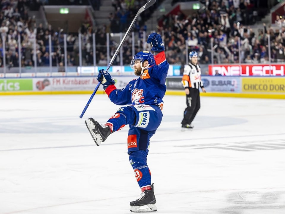 Eishockeyspieler in blauer Uniform jubelt auf dem Eis in einer Arena.