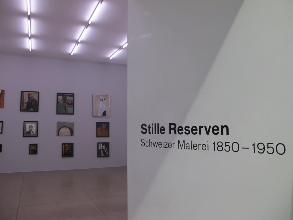 Im Vordergrund die Ausstellungsbeschriftung "Stille Reserven", im Hintergrund eine Wand voller Bilder.