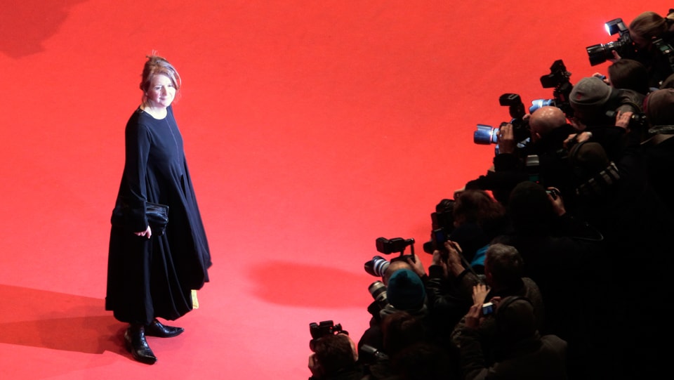 Sally Potter steht auf dem roten Teppich, dementlang die Fotografen dicht gedrängt stehen. 