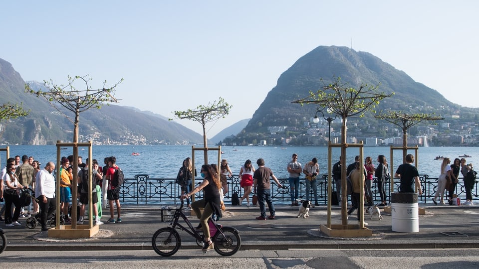 Passantinnen und Passanten geniessen am Seeufer in Lugano das schöne Wetter.