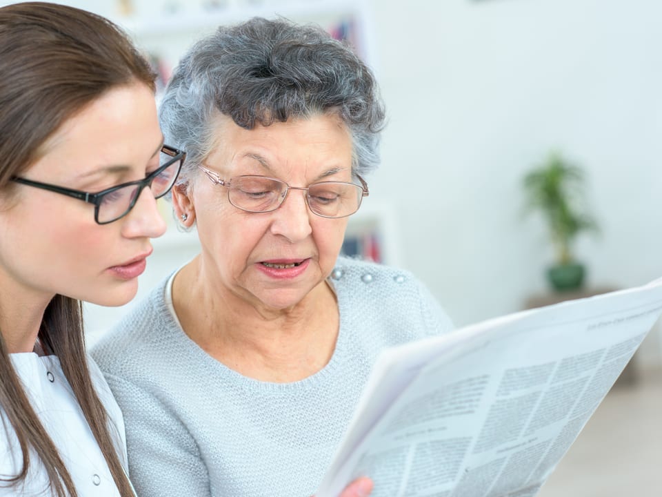 Junge Frau liest mit Seniorin einen Bericht durch. 