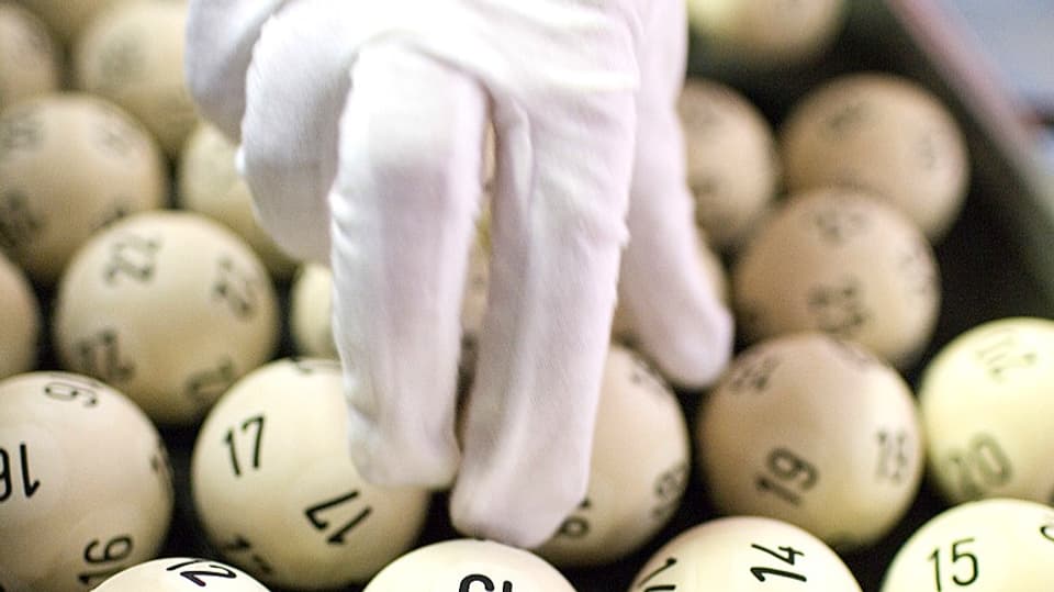 Eine Hand in weissem Handschuh greift in  ein paar Lottokugeln beim Schweizer Zahlenlotto.