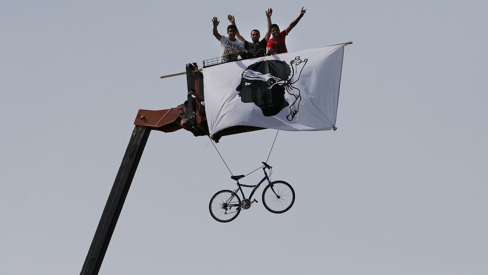 Cycling fans with a flag featuring a Moor's head, the Corsican emblem, cheer as the pack passes during the first stage of the 100th edition of the Tour de France cycling race over 213 kilometers (133 miles) with start in Porto Vecchio and finish in Bastia, Corsica island, France, Saturday June 29, 2013