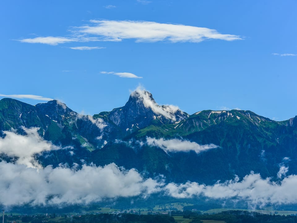 Wolkenreste an den Berghängen, die Gipfel sind von der Sonne beschienen, der Himmel ist teils blau, teils gering bewölkt.