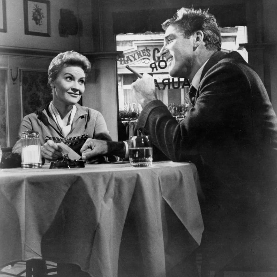 Burt Lancaster und Patti Page am Tisch sitzend.