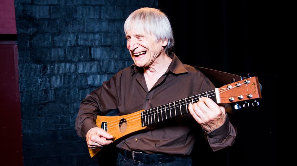 Ein lachender Mann hält ein gitarrenähnliches Instrument.