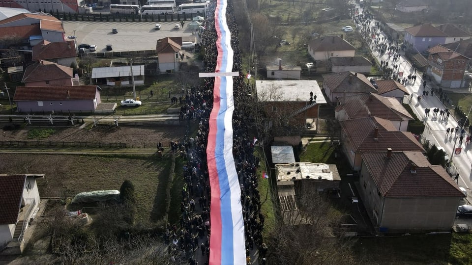 Eine sehr lange serbische Flagge wird wie ein Band durch die Strassen von Mitrovica gezogen