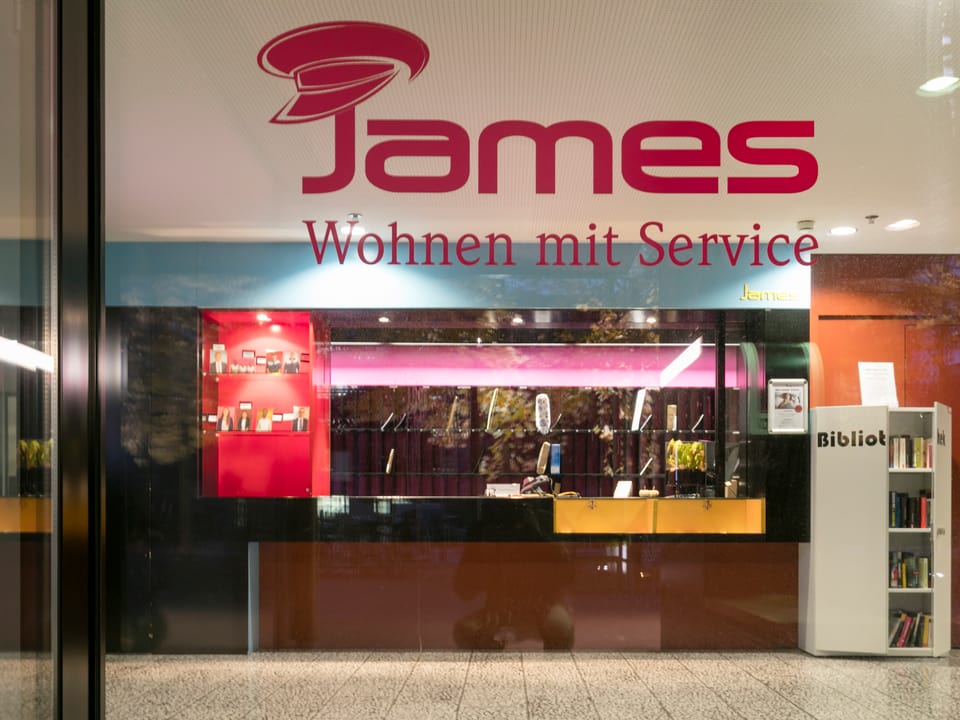 Durch ein Fenster sieht man den Empfang von «James – Wohnen mit Service».