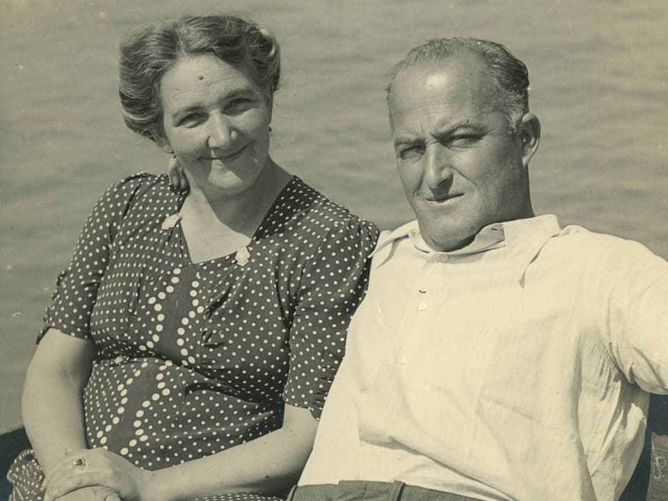 Schwarz-Weiss-Fotografie von einem Ehepaar, das am See sitzt.