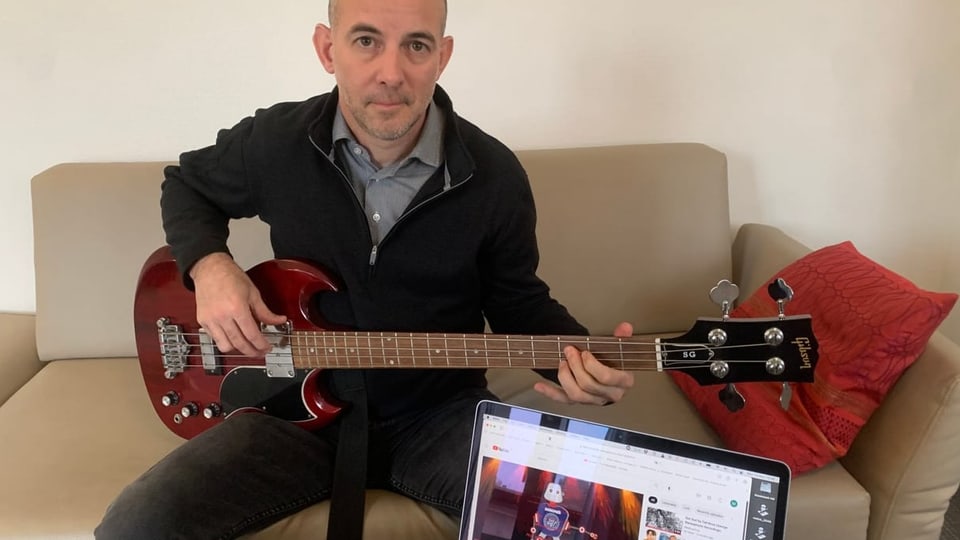 Ein Matthias Frey sitzt auf dem Sofa, mit Gitarre auf dem Schoss und aufgeklappten Laptop vor sich.