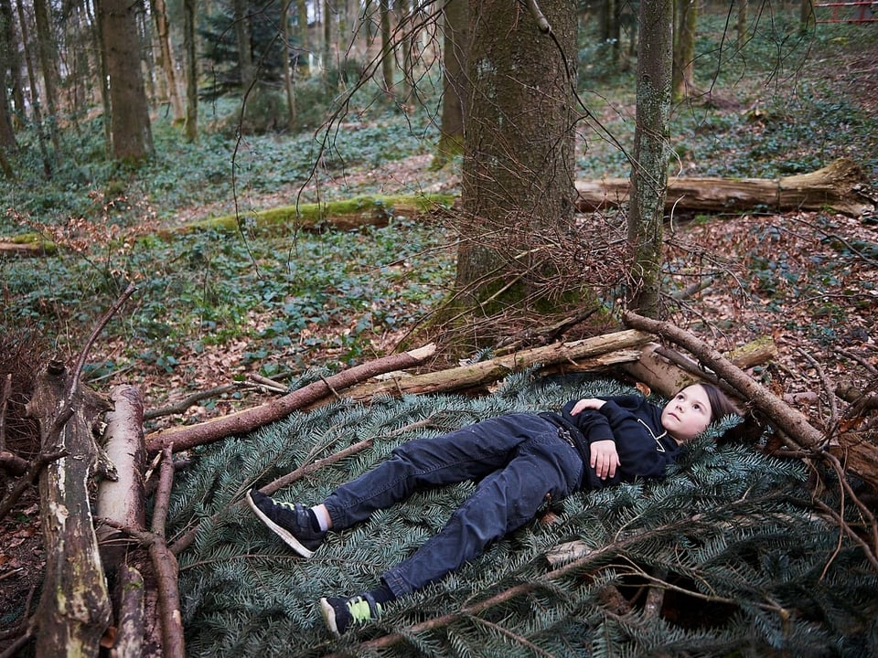 Ein Kind liegt in auf dem Waldboden und blickt in den Himmel.