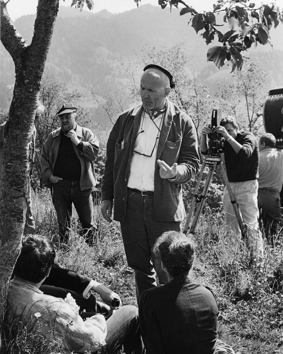 Franz Schnyder gibt Änneli und Christen, welche im Schatten unter einem Baum sitzen, Regieanweisungen. Hinter ihm wird die Kamera aufgebaut.