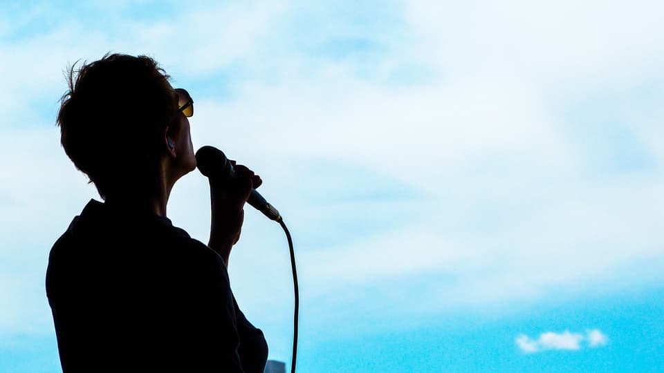 Dunkle Silhouette einer singenden Frau vor blauem Himmel. 