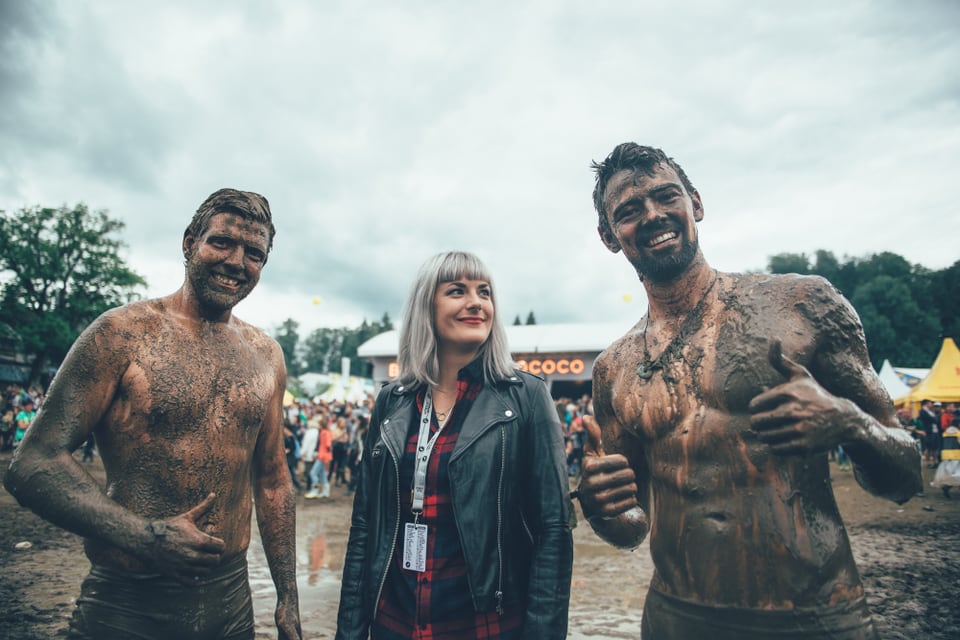 Zwei schlammverschmierte Männer und eine Frau auf einem Festivalgelände