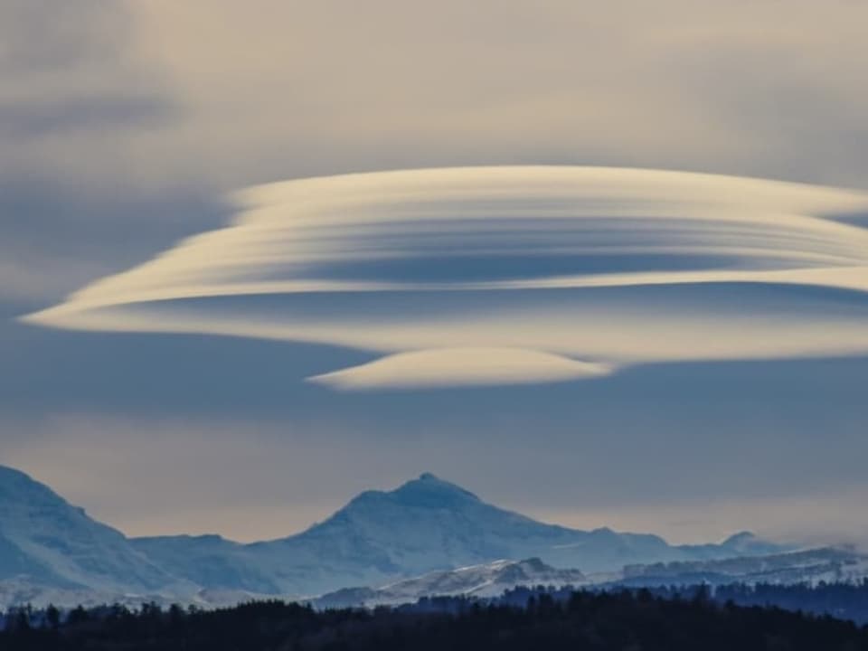 Linsenförmige Wolken über den Alpen mit milchigem Himmel. 