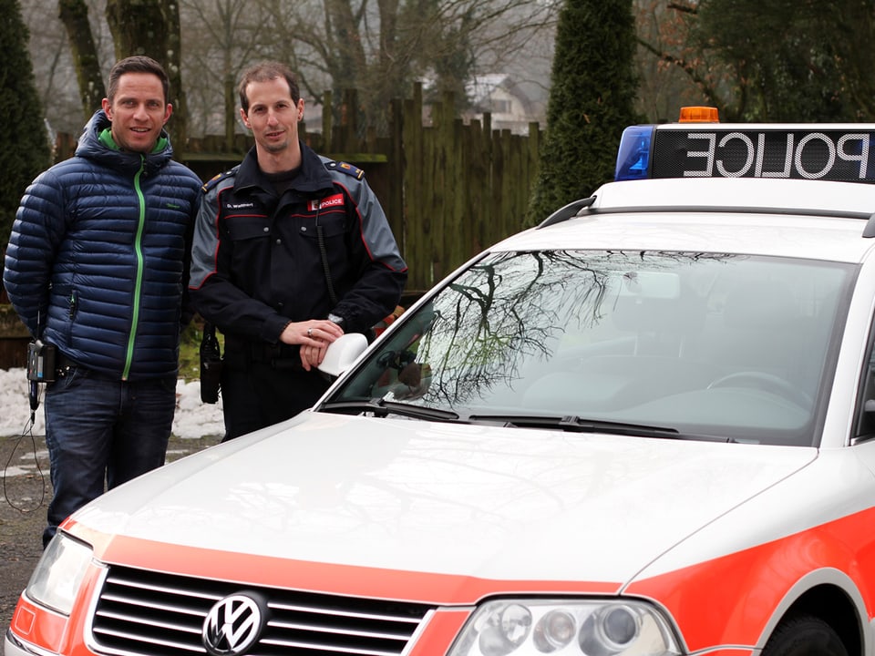 Adrian Küpfer mit einem Polizisten in Uniform neben dem Polizeiauto.