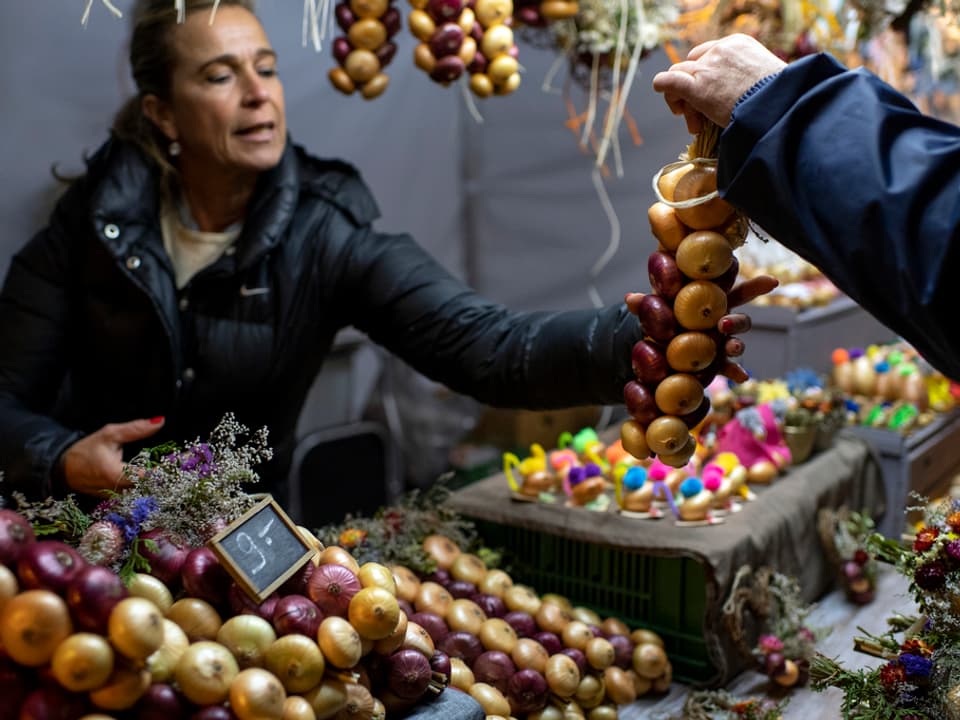 Eine Marktfrau verkauft einen Zwiebelzopf.